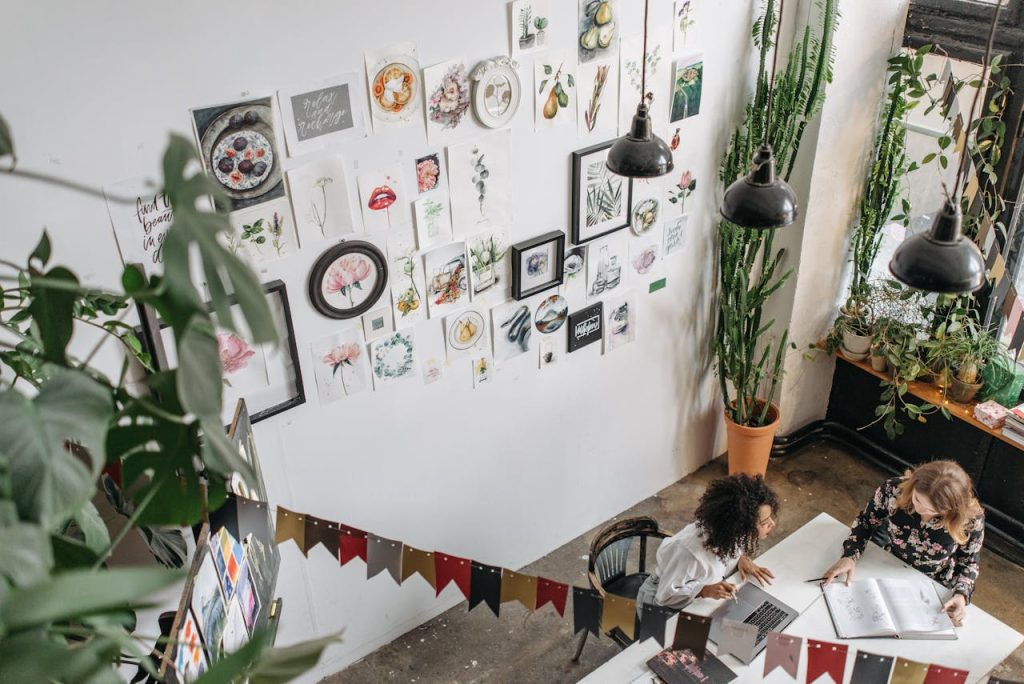 Two women collaborate in a vibrant art studio surrounded by beautiful artwork and plants.